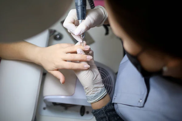 The manicure master processes the client's nails with a nail grinding machine. A manicurist with a device in her hands grinds her nails making preparations for applying nail polish