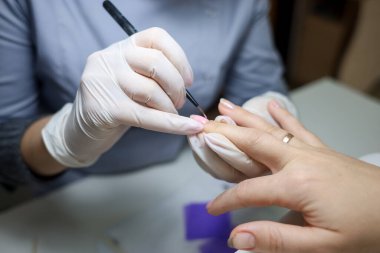 Manikür ustası müşterinin tırnaklarına jel cilası sürüyor. Manikürcü tırnaklarına oje sürmüş.