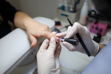 Manikür ustası müşterinin tırnaklarına jel cilası sürüyor. Manikürcü tırnaklarına oje sürmüş.