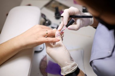 Manikür ustası jel cilasını tırnak yüzeyine eşit olarak dağıtıyor. Manikürcü müşterinin tırnaklarına oje sürmüş..