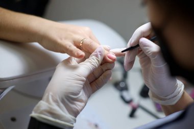 Manikür ustası jel cilasını tırnak yüzeyine eşit olarak dağıtıyor. Manikürcü müşterinin tırnaklarına oje sürmüş..