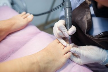 Pedikür ustası tırnak cilası makinesiyle çalışıyor. Pedikürcü müşterinin tırnaklarını hazırlar.