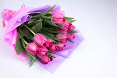 Bir buket şenlikli bahar lalesi Pembe bir ambalaj kağıdına sarılı beyaz bir masada yatıyor