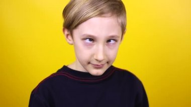 Çocuk gözlerini birleştiriyor ve sonra gülüyor. Çocuk sarı bir arkaplanda duruyor ve duygularını gösteriyor.
