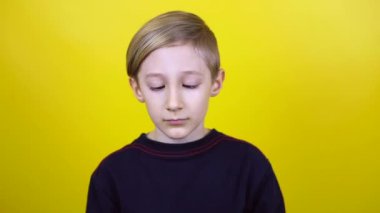 Çocuk gözlerini burnuna koyar ve komik yüzler gösterir. Çocuk sarı arka planda duruyor ve duygularını gösteriyor.