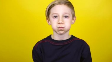 Çocuk derin bir nefes alıyor ve yanaklarını şişiriyor. Çocuk sarı arka planda duruyor ve nefes egzersizleri yapıyor.