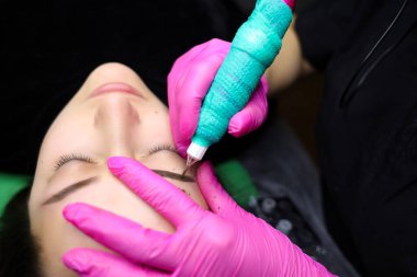 Kalıcı makyaj sanatçısı, dövme prosedürünü uygulamak için kaşların yakınındaki deriyi sıkılaştırır.