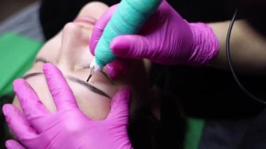 Usta elinde bir dövme makinesi tutuyor ve kalıcı makyaj için bir prosedür uyguluyor.