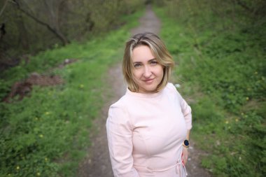 Güzel kız baharda parkta durur ve kameraya bakar.