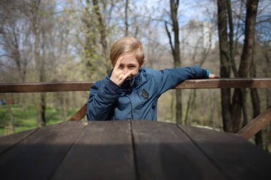 Çocuk bir kafedeki ahşap bir masada oturuyor ve elleriyle çeşitli jestler yapıyor.