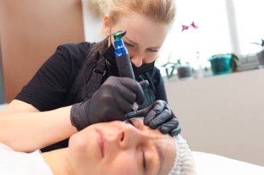 Bir dövme sanatçısı müşteriyi yüzünden tutar ve burada kaş dövmesi yaptırır.