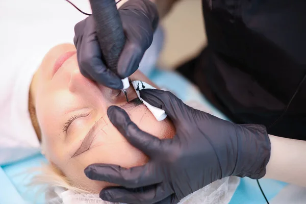 Permanent make-up masters hold a tattoo pen in one hand, and the client\'s eyebrows in the other, so he makes an eyebrow tattoo.