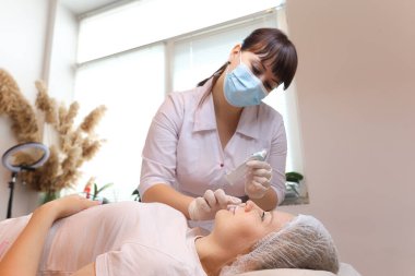 Kozmetik uzmanı anestezi uygular müşterinin dudaklarını hyaluronik asit enjeksiyonuna hazırlar.