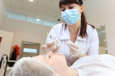 Kozmetik uzmanı yeni bir enjeksiyona hazırlanmak için kızın yüzüne yakın bir yerde hyaluronik asit enjekte ediyor.