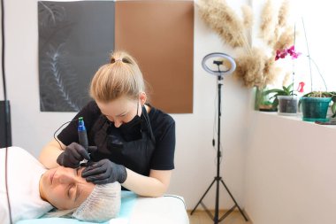 Bir dövme sanatçısı müşteriyi yüzünden tutar ve burada kaş dövmesi yaptırır.