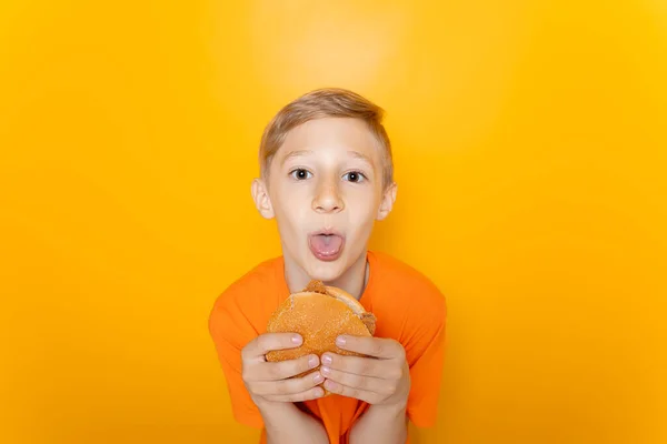 Ein Junge Orangefarbenen Shirt Hält Einen Hamburger Vor Sich Und — Stockfoto