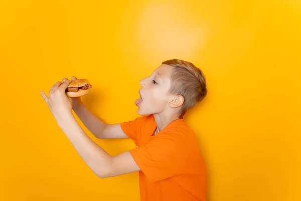 Ein Junge Orangefarbenen Shirt Steht Seitlich Und Hält Einen Hamburger — Stockfoto