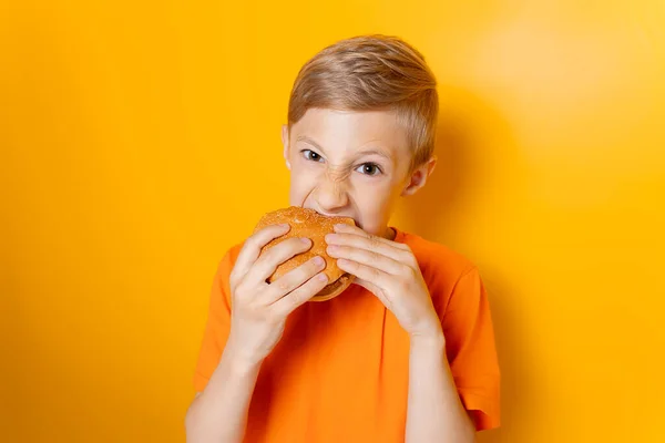 Ragazzo Con Una Maglietta Arancione Tiene Hamburger Entrambe Mani Morde — Foto Stock