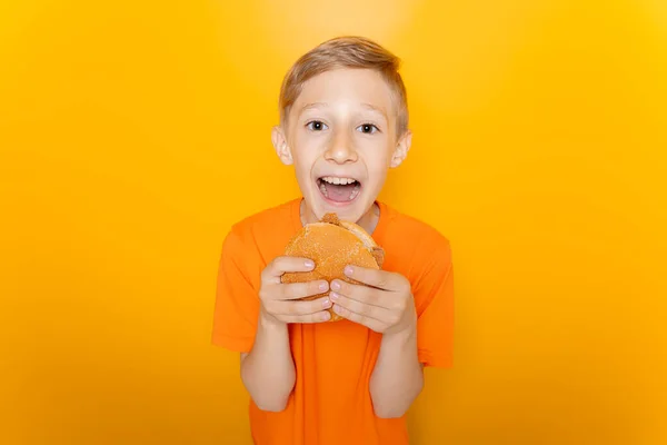 Pojke Orange Shirt Håller Hamburgare Framför Sig Och Skrattar Högt — Stockfoto