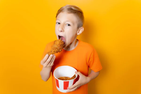 Turuncu Tişörtlü Bir Çocuk Önünde Bir Kova Tavuk Kanadı Tutuyor — Stok fotoğraf