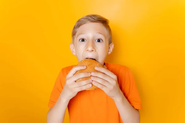 Pojke Orange Shirt Håller Hamburgare Båda Händerna Och Girigt Biter — Stockfoto