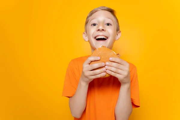 Pojke Orange Shirt Håller Hamburgare Framför Sig Och Skrattar Högt — Stockfoto