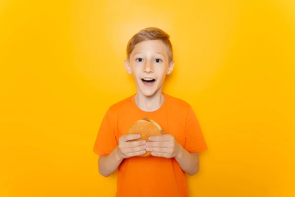 Ragazzo Felice Con Una Maglietta Arancione Alza Piedi Tiene Hamburger — Foto Stock