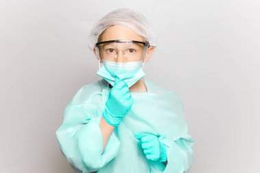 Tıbbi giysili ve maskeli bir çocuk, tek kullanımlık eldiven takan eliyle maskeyi ayarlar.