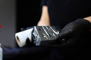 Dövme sanatçısı kalıcı makyaj prosedürüne hazırlanırken pigment tutucuyu bir filmle sarar.