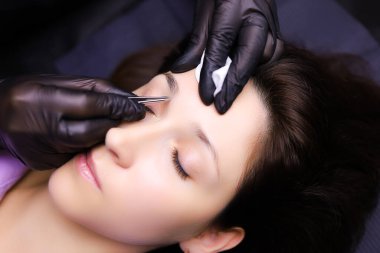 Usta dövme sanatçısı, kaşlarını fazla kılları yolmak için hazırlar. Kaşların dış hatlarını dövme için hazırlar.