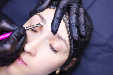 Dövme sanatçısının elleri bir fırçayla kaş çevresini vurgular.