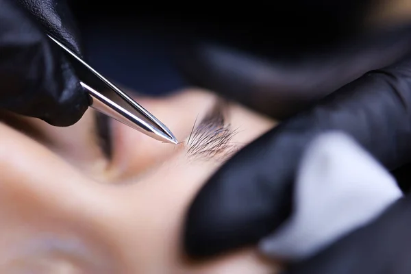 the master of permanent makeup prepares the client\'s eyebrows for the procedure plucking out the hairs with tweezers