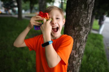 Çocuk sırtı ağaca dönük durur ve gözlerinde bir anti-stres oyuncağı sunar neşeyle güler.
