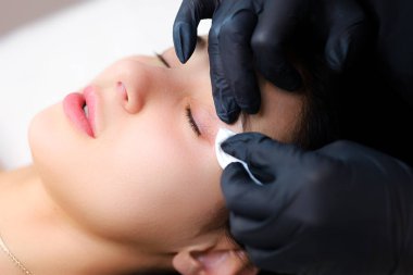 Silia ustası. Elleri müşterinin göz kapaklarını yakın plan çeker ve pamuklu çubukla temizler.