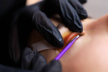 Silia 'nın kaplamasının ustasının ellerini yakın plan çekimde usta kirpikleri kıvırmak için silindire basar ve müşteriye kare şeklinde bakar ve temizler ve mikro fırça atar.