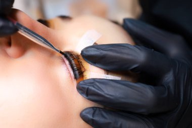 Ustanın ellerinin yakın plan görüntüsü kirpiklerden saç makasına yapışmış bir aletle boyanın kalıntılarını temizliyor.