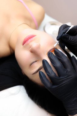 Kız model kozmetik kanepede yatıyor. Silia kaplamasının ustasının elleri. Silia 'yı mankenin göz kapağına kıvırmak için silindiri bastırıyor.