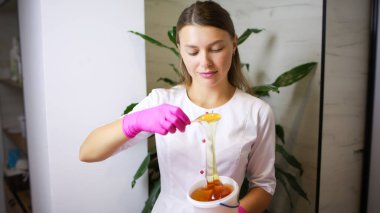 Bir şeker epilasyon ustası spatulayla epilasyon macununu alır..