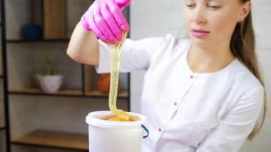 Şekerden kıl kesme ustasının yakın plan çekimi önünde bir kova şeker tutuyordu, elinde sıkıştı ve bu kovanın üzerine kaldırıldı, tutkal bu elden akıyor.