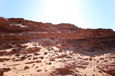 Mavi gökyüzüne karşı kumla kaplı terk edilmiş kırmızı kayalar.