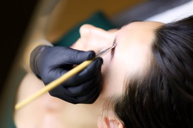 Ustanın yakın çekimi, uzun vadeli kaş şekillendirme işleminden sonra modelin kaşlarını fırçayla tarar.