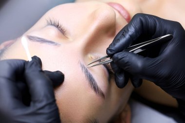 Lekeleme işleminden sonra istenmeyen kaş kıllarının kalıntılarının alınması. Üstat elinde bir cımbız tutuyor ve tüyleri yoluyor.