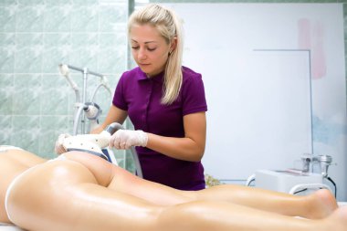 Beyaz külotlu bir model, bir cihazla vakum masajı yapan bir ustanın önünde yatıyor.