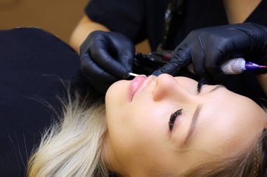 Kalıcı makyaj ustası anesteziyi modelin dudaklarına pamuklu bez ile dağıtır.