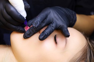 Dövmeci, modelin dudaklarının kalıcı makyajını alt dudağıyla yapar.