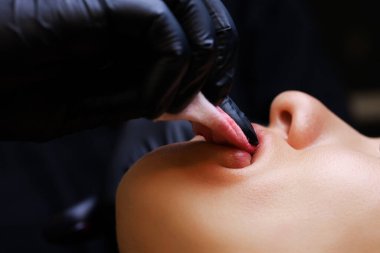 Üstat, dövme modelinin dudaklarındaki kırmızı pigmentleri süngerle siler.