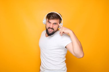 Kulaklıklı sakallı bir adam parmaklarını şakağına uzatmış ve müzik dinliyor..