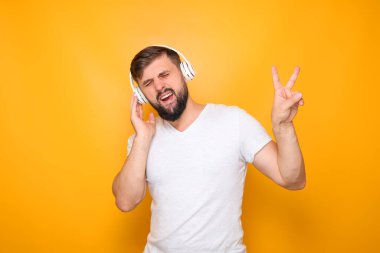 Sakallı, beyaz kulaklıklı bir adam müzik dinliyor ve zafer işareti yapıyor..