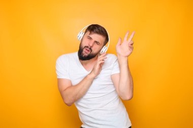 Beyaz tişörtlü ve kulaklıklı sakallı bir adam müziğin ritmiyle dans ediyor..