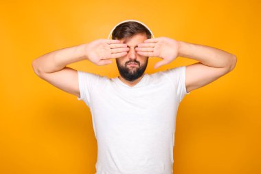 Beyaz kulaklıklı sakallı bir adam, avuçlarıyla gözlerini kapatıyor..